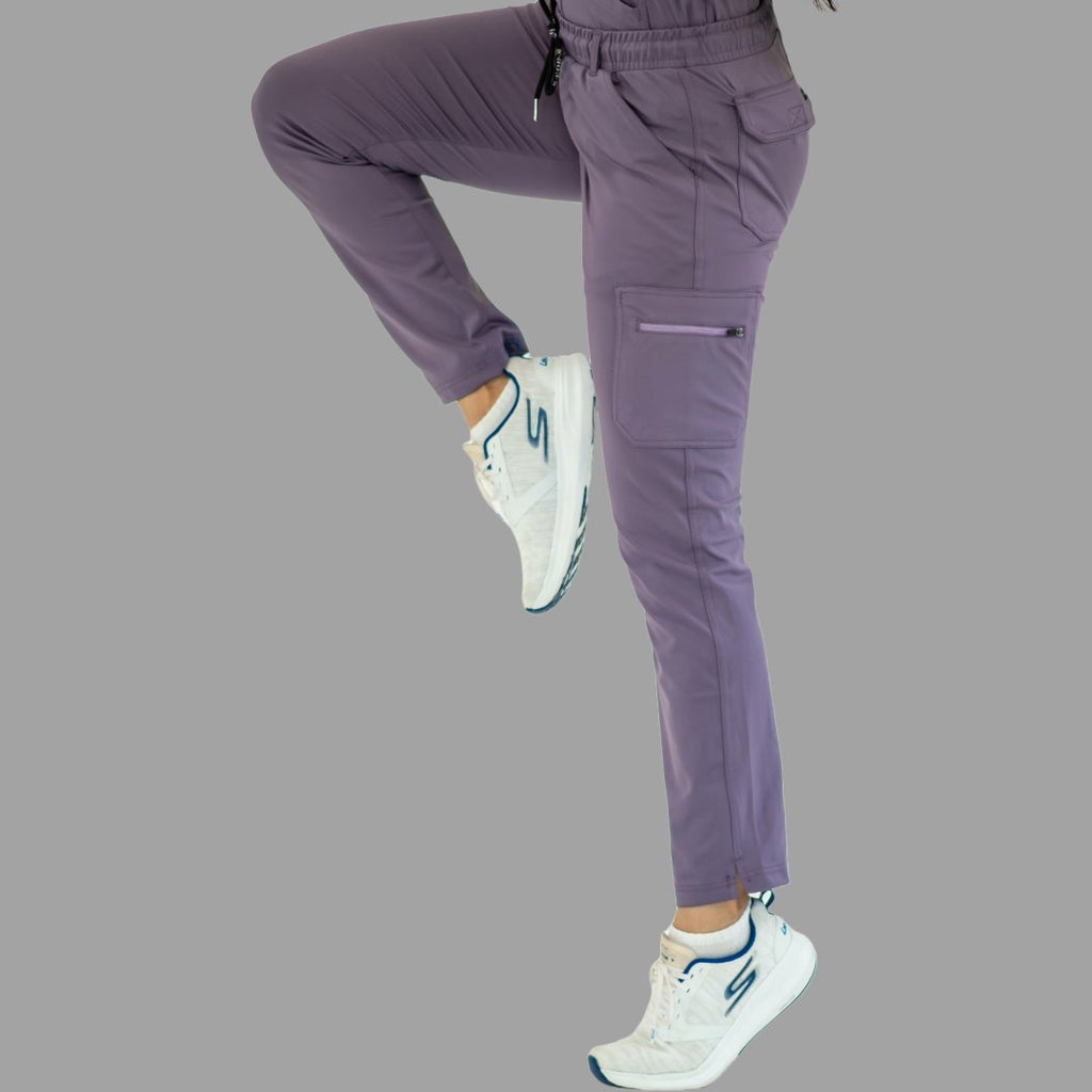 Women's light purple Style 930 scrub pants, dynamic pose with one leg raised showing flexibility.